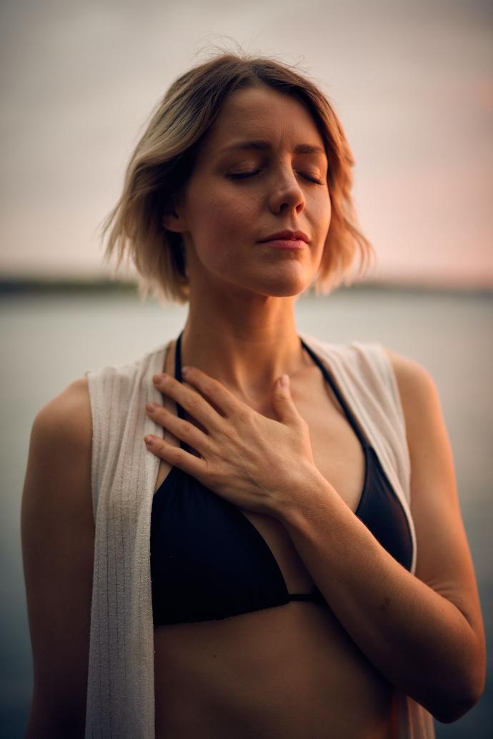 Ervaring Alexadra woman in white vest and black bikini with hand on chest